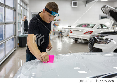 Professional skilled male master in car service applying armor film to hood 106697070