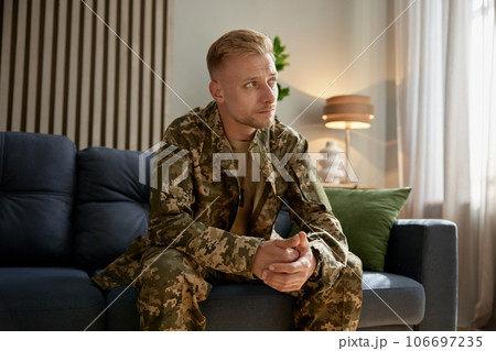 Depressed veteran wearing military uniform sitting on couch feeling upset 106697235