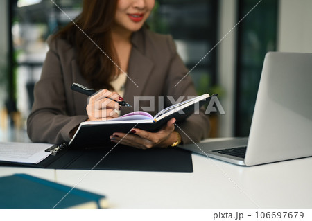 Cropped shot of businesswoman using laptop and writing notes in personal daily planner 106697679