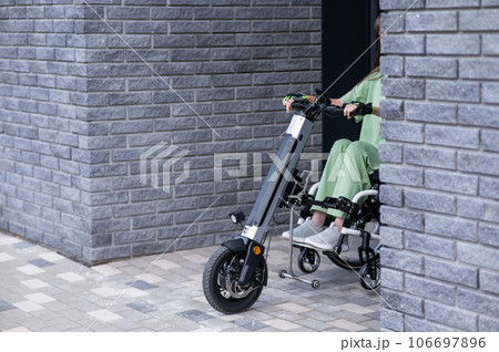 A woman in a wheelchair with a manual assist device comes around the corner. Electric handbike. A woman in a wheelchair with a manual assist device comes around the corner. Electric handbike. 106697896