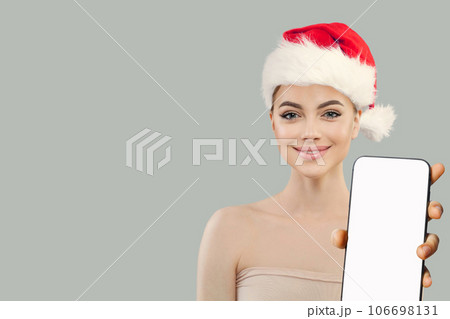 Christmas woman. Cheerful Santa model showing smartphone with empty white screen display, Christmas woman. Cheerful Santa model showing smartphone with empty white screen display, 106698131