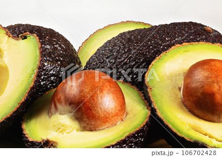 Detail of avocado halves, yellow and green pulp with dark skin - Hass / Bilse variety - pit visible in halved pears Detail of avocado halves, yellow and green pulp with dark skin - Hass / Bilse variety - pit visible in halved pears 106702428
