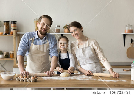Happy young parents and girl in aprons baking together 106703251