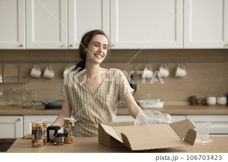 Happy pretty adult girl unpacking cardboard box with canned vegetables 106703423