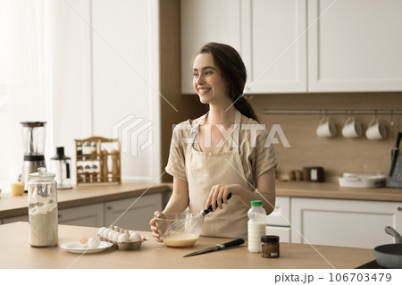 Happy dreamy pretty young woman cooking homemade breakfast in kitchen 106703479