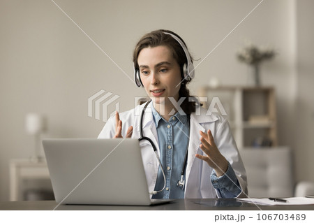 Serious doctor in white coat and headphones speaking at laptop 106703489