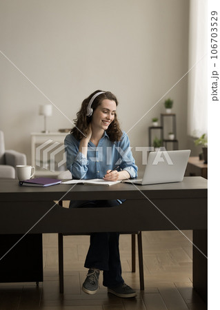 Cheerful college student girl in earphones writing notes at laptop 106703529