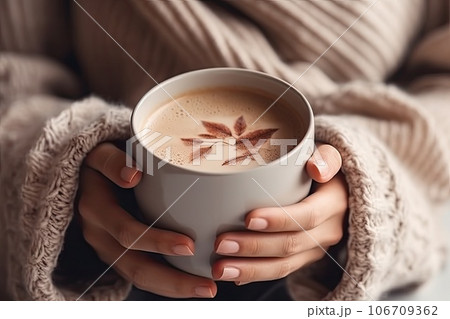 a woman holding a cup of hot chocolate latte in her hands, with a leaf drawn on the foam 106709362