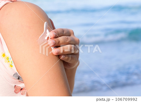 A woman is applying sunscreen and skin care to protect her skin from UV rays. She is applying sunscreen on her shoulder . The sun symbol is a very sunny background. Health and skin care concept 106709992