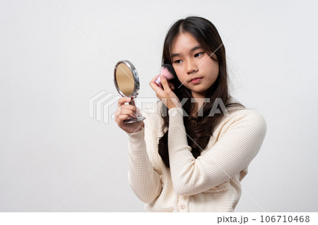 Beautiful young woman makes blush on her face using makeup brush on isolated white background. Teenage girl doing her own makeup. Close up portrait. Copy, empty space for text 106710468