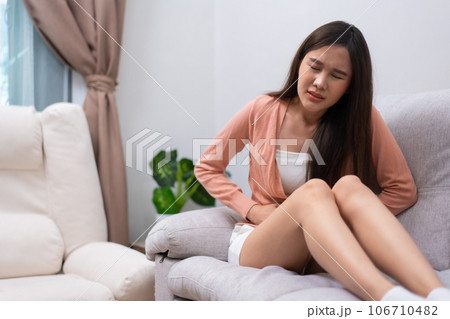 Sick Asian Woman Suffering From Acute Abdominal Pain in the abdomen due to menstruation period, PMS.  Sitting On Couch, stomachache from food poisoning, abdominal pain, digestive problem, gastritis 106710482