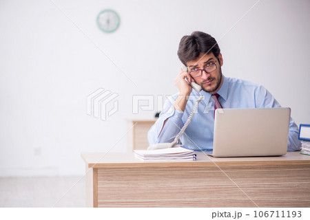 Young male employee talking by phone at workplace Young male employee talking by phone at workplace 106711193