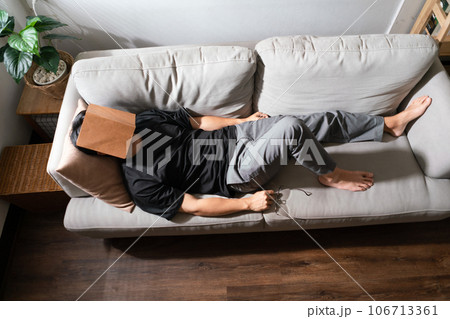 Man with mental health problem lying on comfortable couch and covering face with book to sleeping 106713361