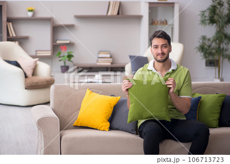 Young man with a lot of pillows sitting on the sofa Young man with a lot of pillows sitting on the sofa 106713723