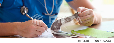 Male doctor reading patient's medical history and taking notes while working at office desk. Male doctor reading patient's medical history and taking notes while working at office desk. 106715288