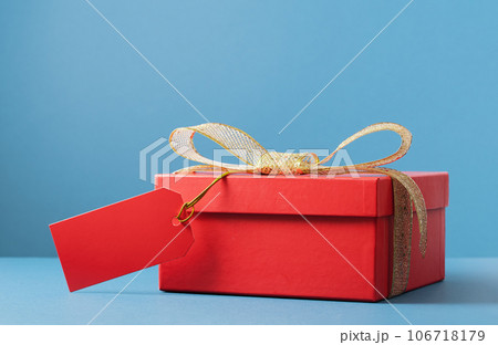 red gift box on blue background. Golden bow and mockup gift tag. Holiday shopping and delivery or sale and discount concept red gift box on blue background. Golden bow and mockup gift tag. Holiday shopping and delivery or sale and discount concept 106718179