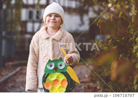 Little preschool kid girl holding selfmade traditional owl lanterns with candle for St. Martin procession. child happy about children and family parade in kindergarten. German tradition Martinsumzug 106718707