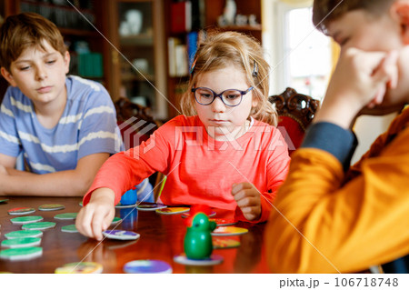 Family playing board game at home. Kids play strategic game. Little sister girl and two school brothers boys. Fun indoor activity. Siblings bond. Educational toys. 106718748