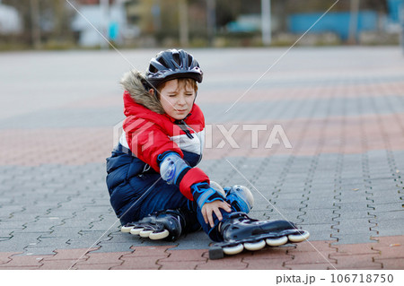 Little school kid boy skating with rollers in the city. child in protection safety clothes. Active schoolboy making sports and learning to skate on inline skater. Falling down and getting hurt 106718750