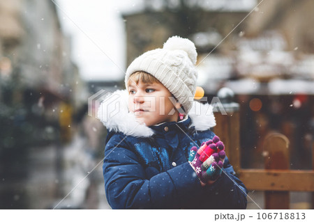 Little cute preschool girl on Christmas market. Happy child on traditional family market in Germany. Preschooler in colorful winter clothes during snowfall 106718813