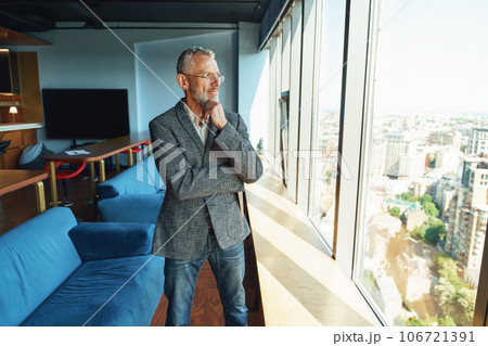 Pensive senior manager looking at window while standing in modern coworking near window 106721391