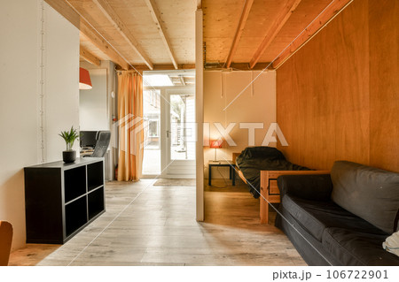 a living room with wood paneled walls and black couch in the center of the room, there is a tv on the wall 106722901