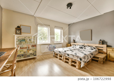 a bedroom with wood flooring and white walls, including a bed made out of wooden pallets on the wall 106722998