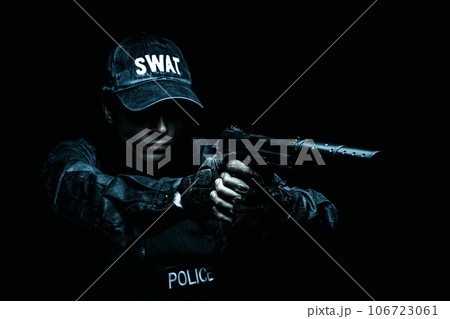 Spec ops police officer SWAT in black uniform aiming pistol with silencer, studio shot, half length 106723061