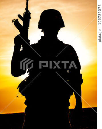 Silhouette of US soldier with rifle at sunset standing as the sun sets in the background 106723078