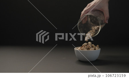 man pour roasted salted pistachios into white bowl on black paper background 106723159
