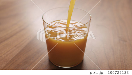 Pour orange juice in thin wall glass on wood table 106723188