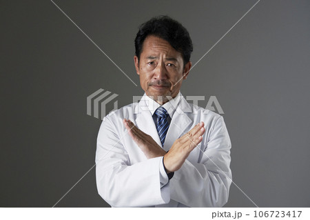 腕でばつ印のジェスチャーをする中年の医師 黒背景 腕でばつ印のジェスチャーをする中年の医師 黒背景 106723417