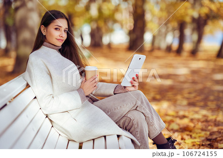 Young  beauty woman sitting with a cup of coffee on a bench in the fall park 106724155