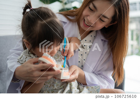 Asian female dentist teaching cute little girl brushing teeth with toothbrush and stomatologist telling girl child about oral hygiene in dental clinic, Education and prevention cavities concept. Asian female dentist teaching cute little girl brushing teeth with toothbrush and stomatologist telling girl child about oral hygiene in dental clinic, Education and prevention cavities concept. 106725610