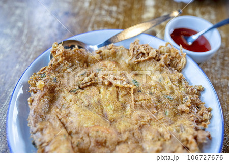 Close-up shallow field of view of Thai style omelet by mixing eggs with coriander and stirring well Fry in hot oil until the egg is cooked, yellow, fragrant, with a small cup of tomato sauce. 106727676