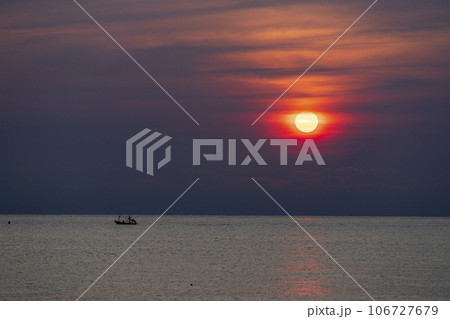 Distant photo of a small boat and an identifiable fisherman in silhouette. Sailing on the sea near the horizon There is a rising or setting sun,depending on the viewer's interpretation and application 106727679