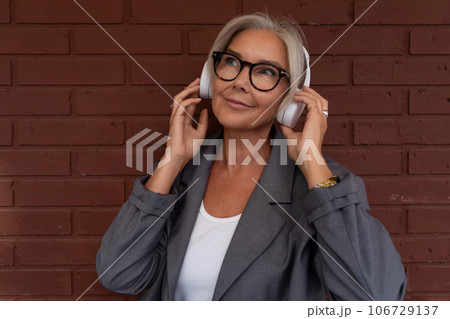 a well-groomed senior woman with gray hair and glasses is dressed in a gray jacket and jeans 106729137