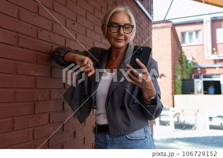 gray-haired mature dreamy woman dressed in a stylish gray jacket and jeans walks and enjoys the gray-haired mature dreamy woman dressed in a stylish gray jacket and jeans walks and enjoys the 106729152
