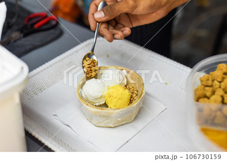 Hand holding coconut and mango ice cream in coconut shell in Jalan Alor street food market in Kuala Lumpur Hand holding coconut and mango ice cream in coconut shell in Jalan Alor street food market in Kuala Lumpur 106730159