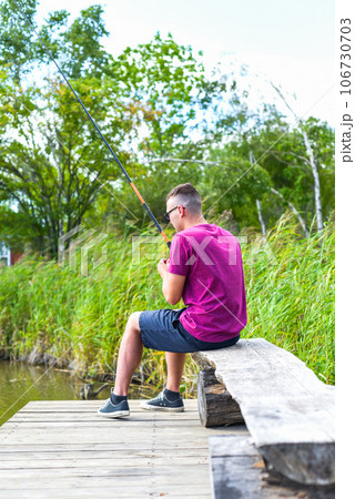 Young fisherman sitting on wooden pier, fishing in the lake. he holding the rod and looking at float 106730703