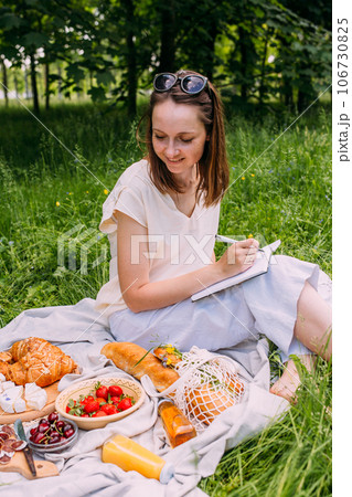 Beautiful woman on picnic. She smiles, eats strawberries and enjoys summer. 106730825