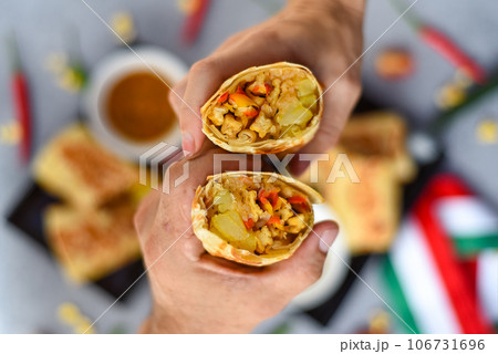 Hands holding vegetarian Mexican burritos with potato, tofu,rice served with sauce brracha Hands holding vegetarian Mexican burritos with potato, tofu,rice served with sauce brracha 106731696