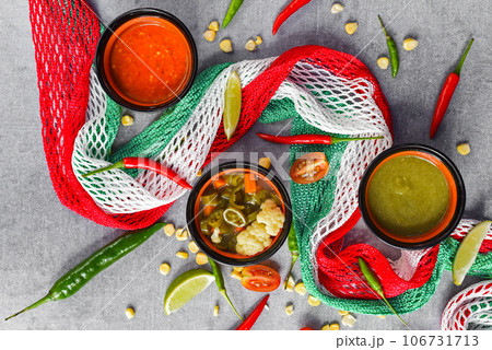Three mexican sauces with vegetables and mexican flag on gray background Three mexican sauces with vegetables and mexican flag on gray background 106731713