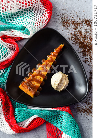 Tlatelolco cake or Corn cake with coffee ice cream on black plate with Mexican flag Tlatelolco cake or Corn cake with coffee ice cream on black plate with Mexican flag 106731717