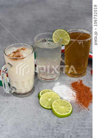 Mexican drinks Horchata water, Lime juice and beer on a gray table with salt pepper and lime 106732019