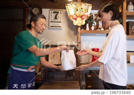レジにて女性客に商品を手渡す男性店主 レジにて女性客に商品を手渡す男性店主 106733680