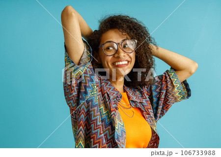 Pretty woman in eyeglasses standing with raised hands on blue studio background and looks away 106733988