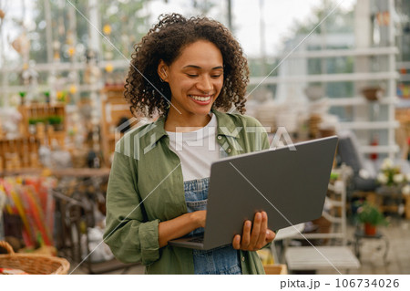 Female gardening shop owner working on laptop on garden store center background Female gardening shop owner working on laptop on garden store center background 106734026