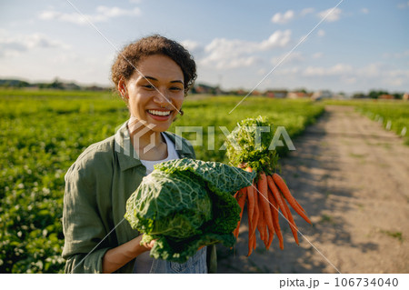 Smiling female farmer standing with just harvested vegetables on the field background Smiling female farmer standing with just harvested vegetables on the field background 106734040
