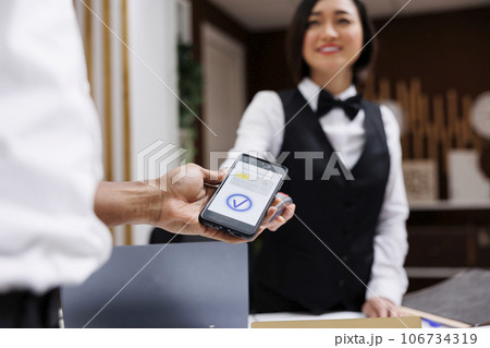 African american man using phone nfc to pay for room booking at reception counter, front desk. Young guest paying on pos terminal, electronic payment at check in registration. Close up. African american man using phone nfc to pay for room booking at reception counter, front desk. Young guest paying on pos terminal, electronic payment at check in registration. Close up. 106734319